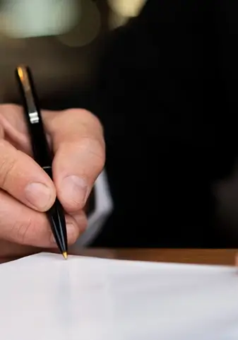 zdjęcie przedstawiające człowieka piszącego coś długopisem na kartce z trochę oddalonej prespektywy
